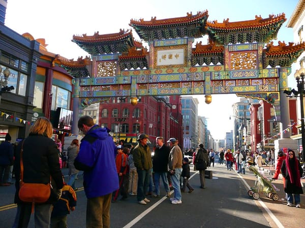 A crowd stands beneath the arches in Chinatown on a sunny day. 