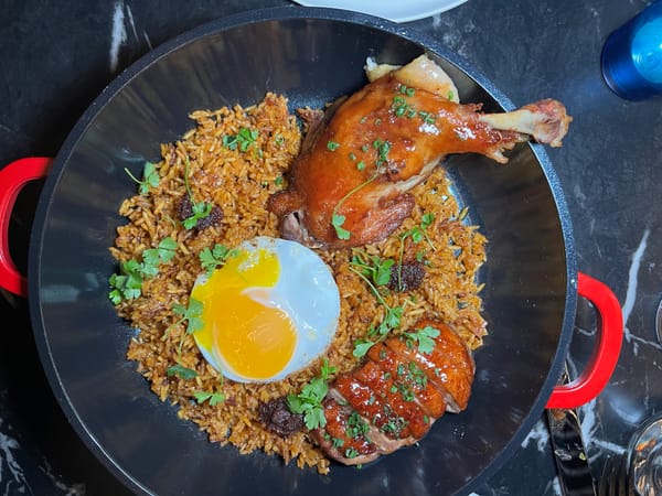 A bowl of jollof rice with an egg and meats. 