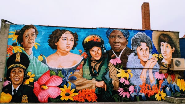 A photo of a mural depicting seven women, with a backdrop of blue with white stars.