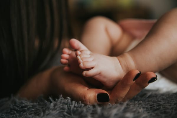 A baby's tiny feet are being held in someone's hand with black fingernail polish.