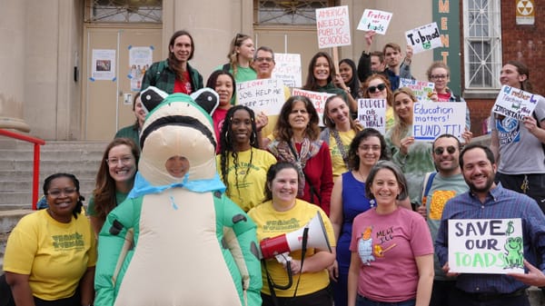 Teachers hold signs and pose for a photo on the stairs in front of Tubman Elementary