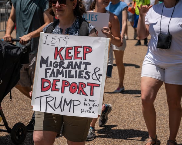 Someone in a protest holds a sign that says Let's Keep Migrant Families & Deport Trum
