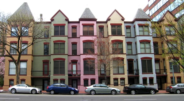 A colorful row of four-story row houses with cars parked on the street. 