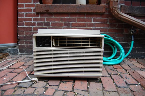 A window AC unit sitting on brick. 