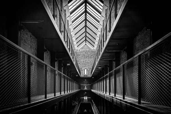 Interior of a row of prison cells, in black and white.
