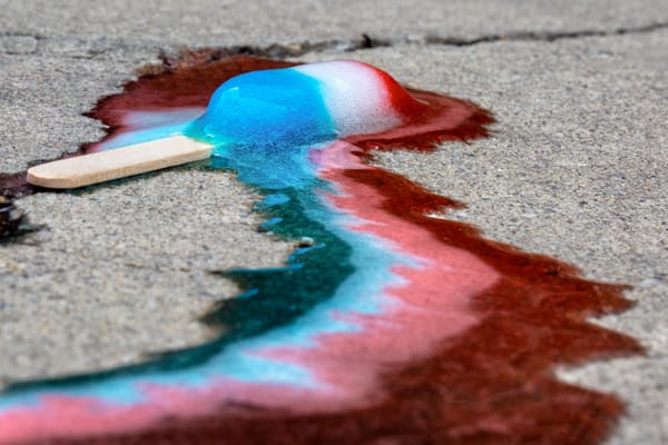 A red, white, and blue popsicle melting on the ground. 