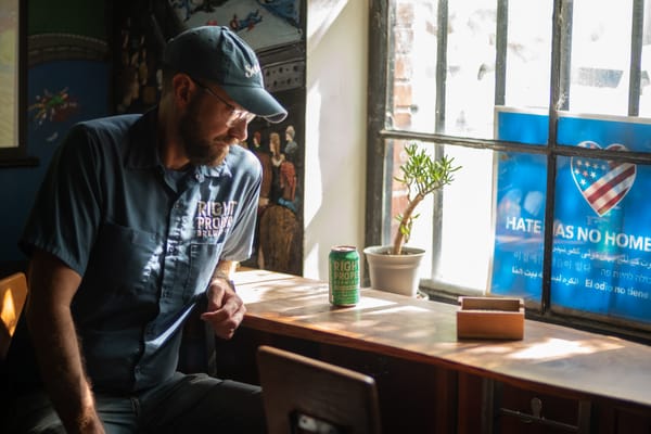 A man in a Right Proper Brewer jumpsuit and hat looks down at a can of beer on a table. 