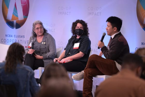 Three people sit in chairs on stage, with one speaking into a microphone.